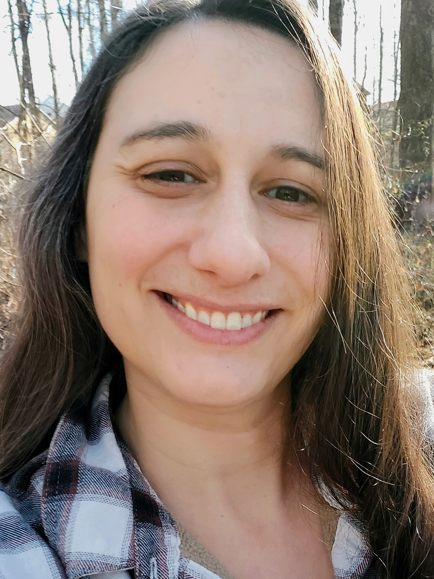 Metaworker editor Mel Reynolds (light skin, long dark hair) smiles at the camera in a close-up. She is wearing a black and white plaid, collared blouse.