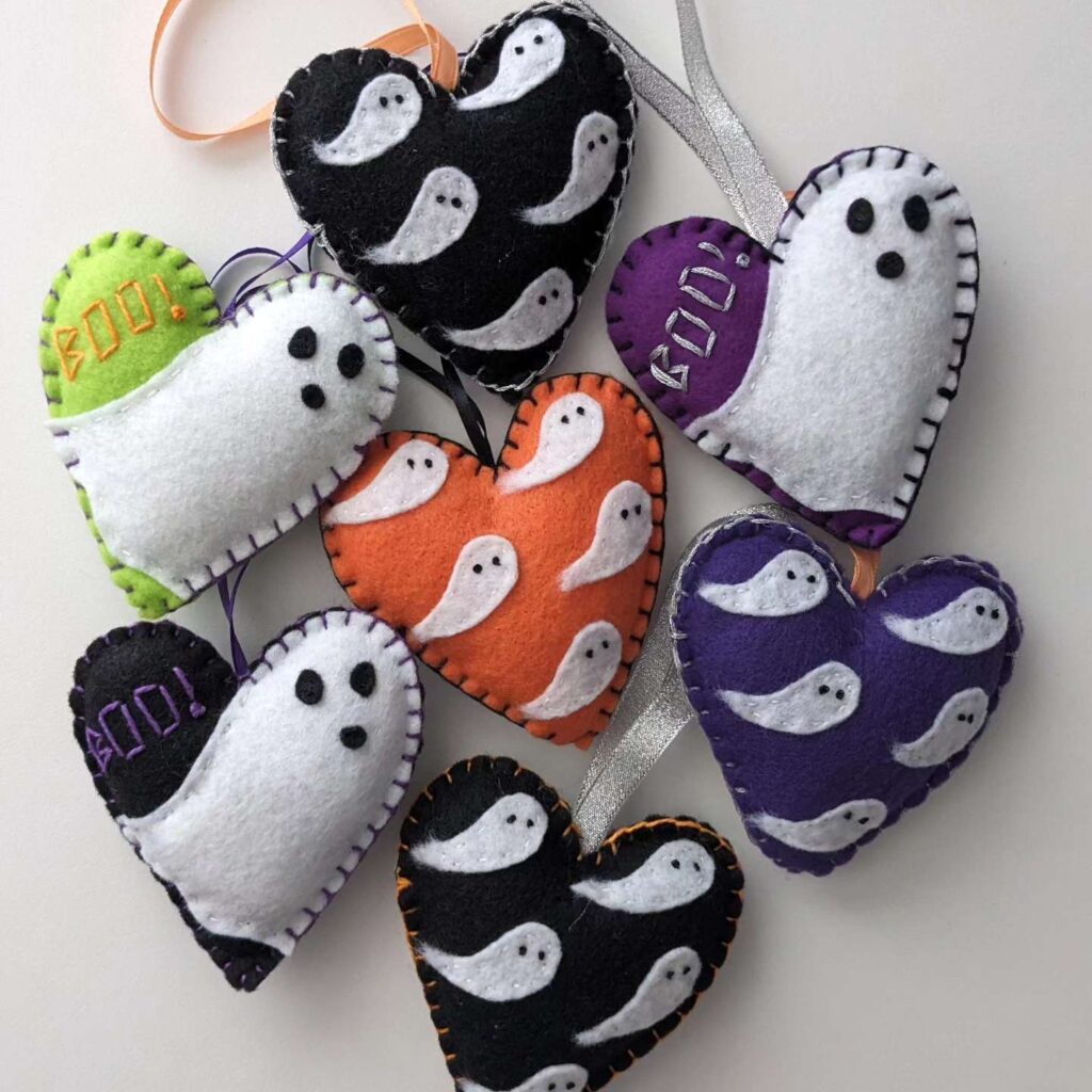 Ghost ornaments, hand-sewn by Elena: A colorful cluster of eight heart-shaped felt ornaments with embroidered ghosts, including black hearts, purple hearts, an orange heart, and hearts with the word "BOO!"