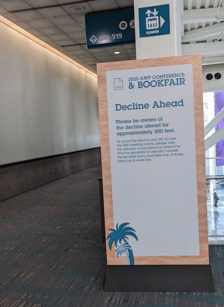 AWP 2025 sign detailing a ramp's grade of decline. It is a tall sign standing on the floor that is pictured next to the ramp it references.