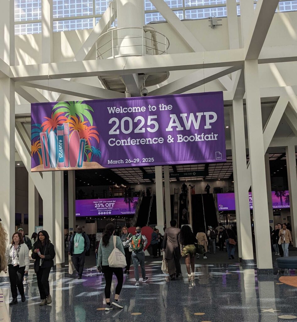 A large purple AWP 2025 Welcome Banner hanging over the foyer in the Los Angeles convention center with people walking underneath.